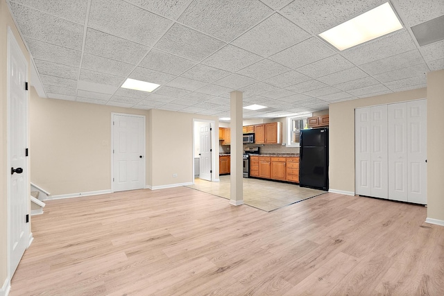unfurnished living room with a drop ceiling, light wood-style flooring, and baseboards