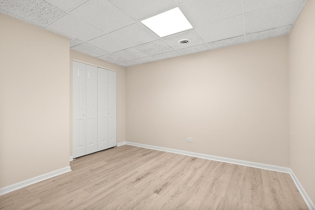 unfurnished bedroom with light wood finished floors, a paneled ceiling, baseboards, and a closet