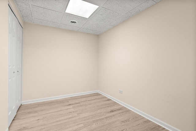 spare room featuring light wood finished floors, baseboards, and a paneled ceiling