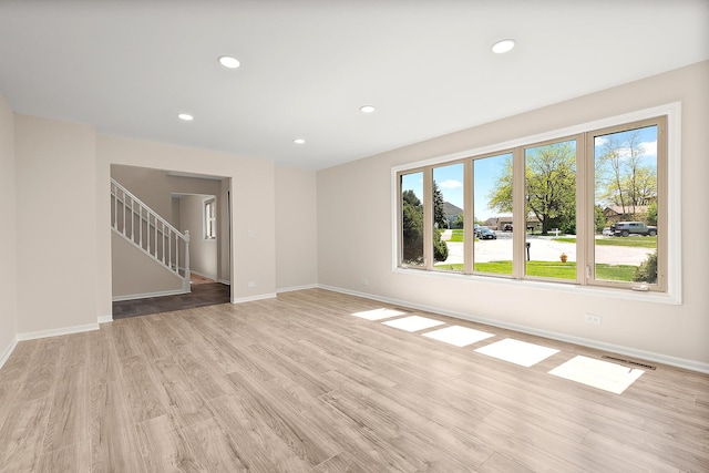 spare room featuring baseboards, recessed lighting, light wood-type flooring, and stairs