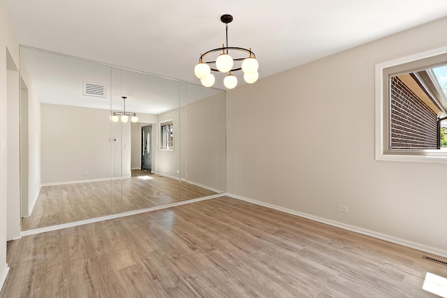 spare room featuring a chandelier, light wood-style flooring, and baseboards