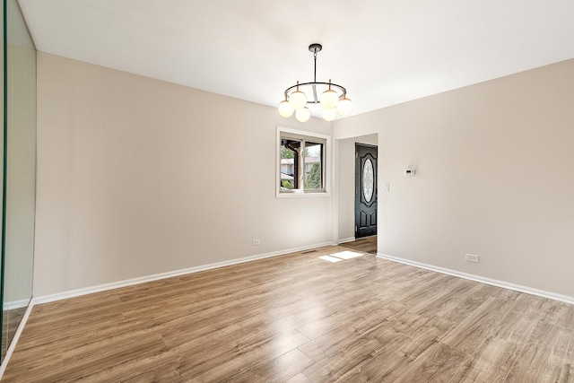 unfurnished room with a chandelier, light wood finished floors, and baseboards