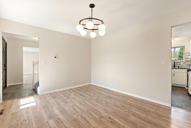 spare room featuring light wood-style flooring, a chandelier, stairs, and baseboards