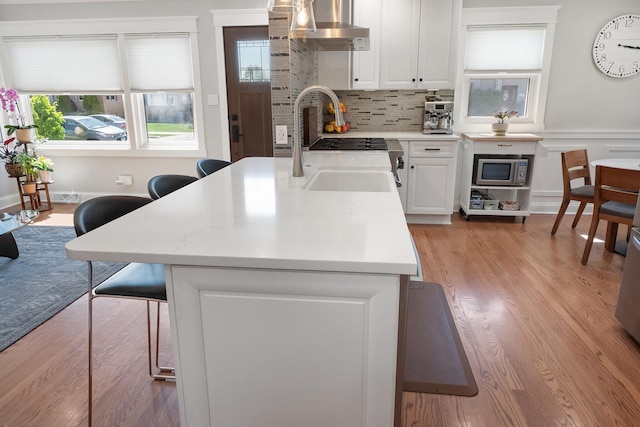 4937 N Opal Ave, Norridge, IL 60706 - kitchen with wall chimney range hood, stainless steel microwave, light wood-style flooring, a breakfast bar area, and a sink