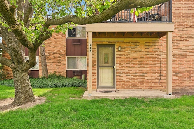 entrance to property featuring a balcony, a yard, and brick siding