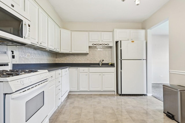 kitchen featuring white appliances, a sink, white cabinets, backsplash, and dark countertops