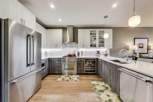 kitchen with high quality appliances, wall chimney range hood, wine cooler, a sink, and light wood-type flooring