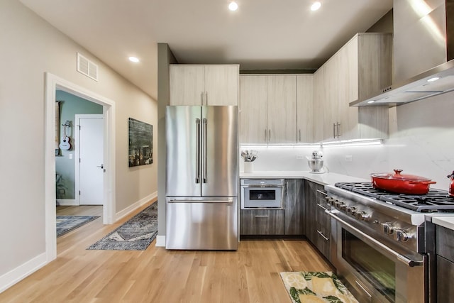 kitchen with high end appliances, wall chimney exhaust hood, light wood-style flooring, light countertops, and recessed lighting