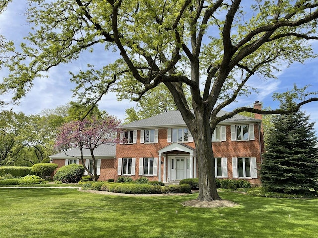 colonial-style house featuring a front lawn, brick siding, and a chimney