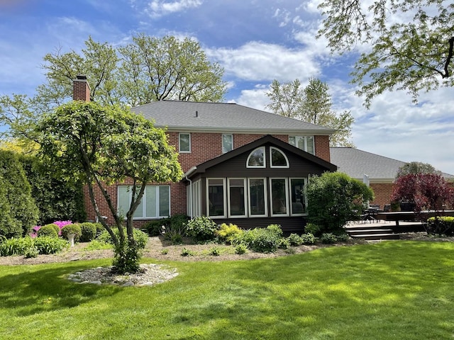 rear view of house featuring a yard, brick siding, a chimney, and a deck