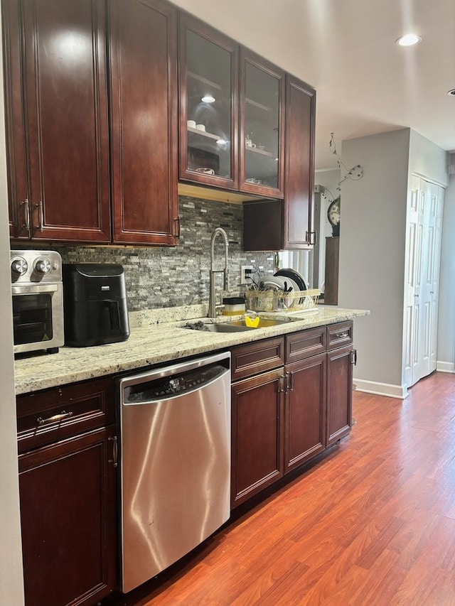 kitchen featuring dishwasher, a sink, backsplash, wood finished floors, and light stone counters