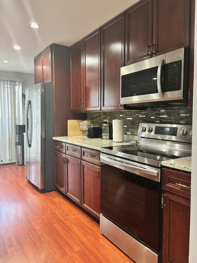 kitchen featuring stainless steel appliances, backsplash, light wood-style flooring, light stone counters, and recessed lighting