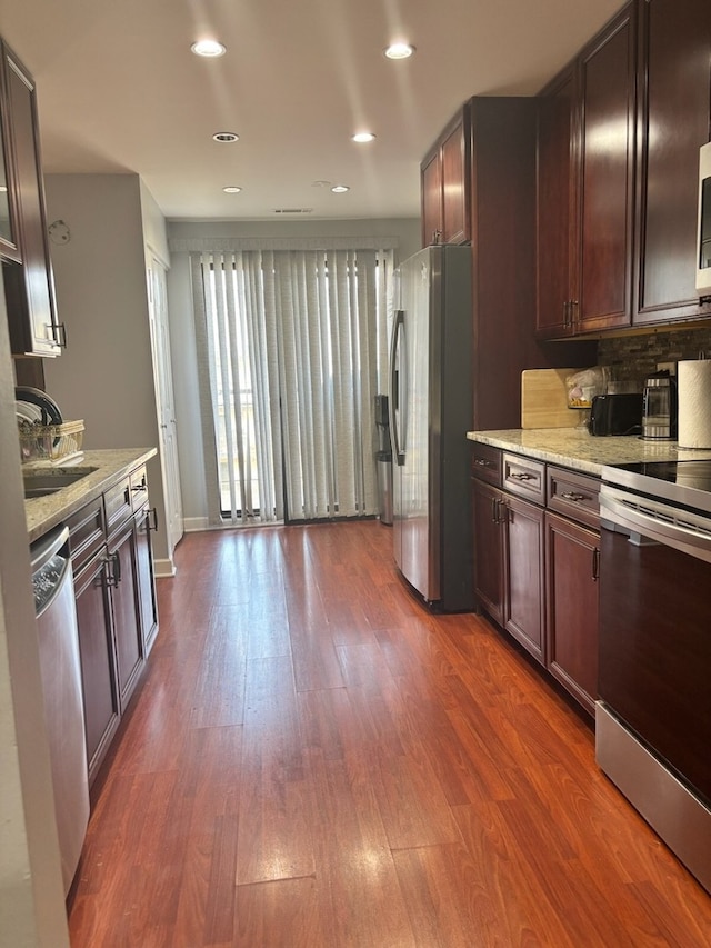kitchen featuring stainless steel appliances, a sink, light stone counters, recessed lighting, and dark wood finished floors