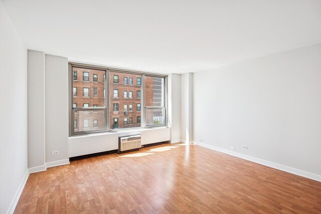 unfurnished room featuring light wood-style floors, baseboards, and a wall mounted air conditioner