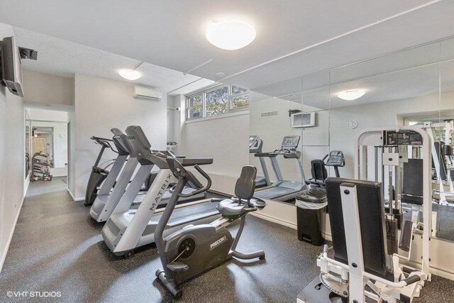 exercise room with a wall mounted AC and baseboards