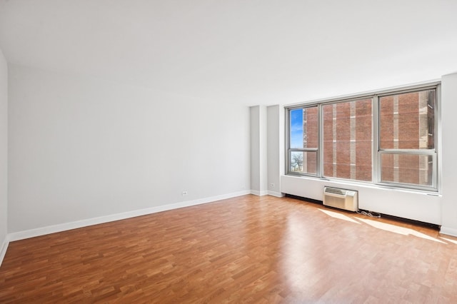 spare room with wood finished floors, baseboards, and an AC wall unit