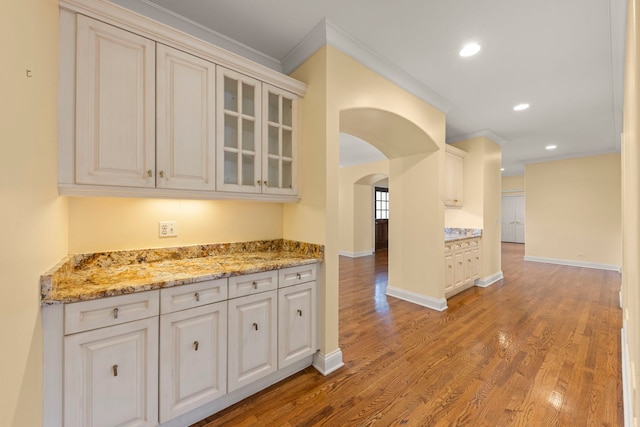 1161 Gavin Ct, Lake Forest, IL 60045 - kitchen featuring ornamental molding, arched walkways, glass insert cabinets, light wood-type flooring, and light stone countertops
