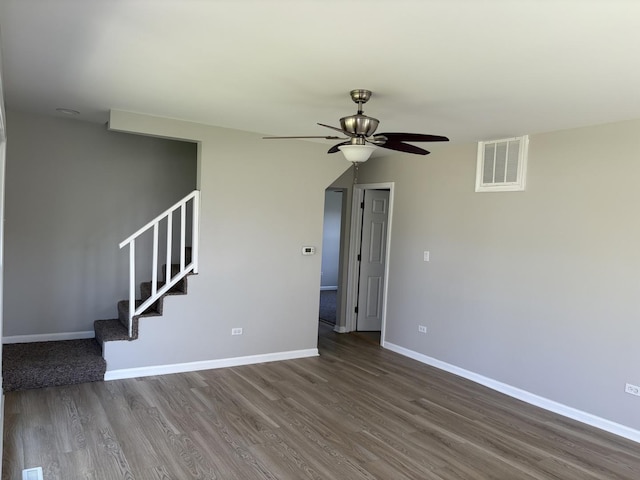unfurnished living room with a ceiling fan, dark wood finished floors, baseboards, and stairway