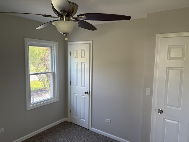 empty room with ceiling fan, dark carpet, and baseboards