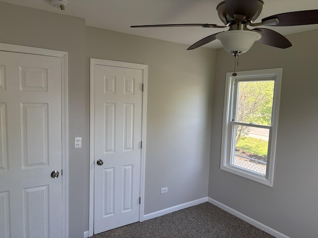 unfurnished bedroom featuring dark colored carpet, baseboards, and a ceiling fan