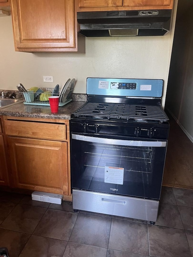 3118 W Douglas Blvd, Chicago, IL 60623 - kitchen with stainless steel gas range, under cabinet range hood, dark countertops, dark tile patterned floors, and brown cabinetry