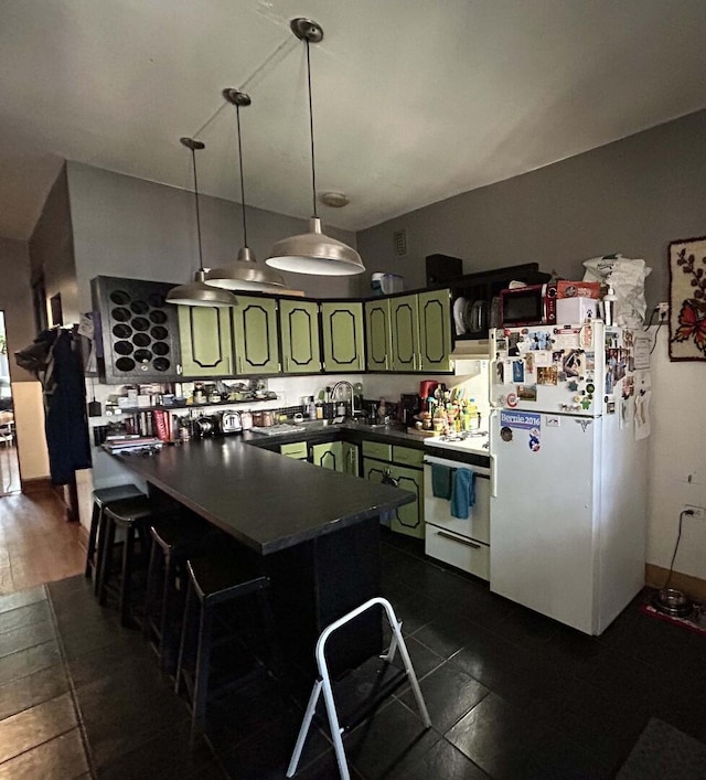 kitchen with white appliances, green cabinets, dark countertops, a kitchen bar, and hanging light fixtures