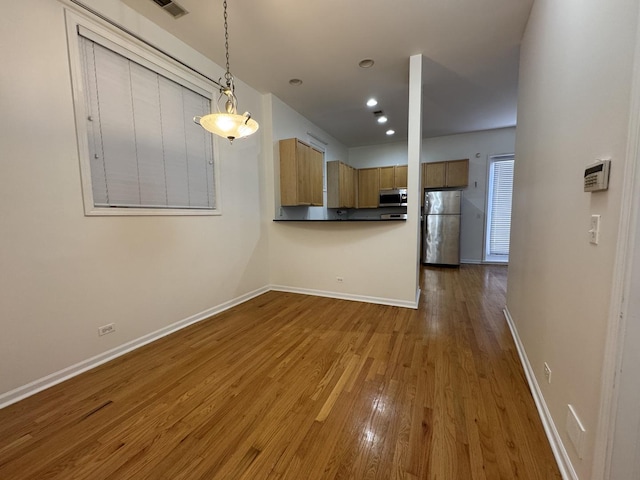 kitchen featuring appliances with stainless steel finishes, brown cabinets, baseboards, wood finished floors, and hanging light fixtures