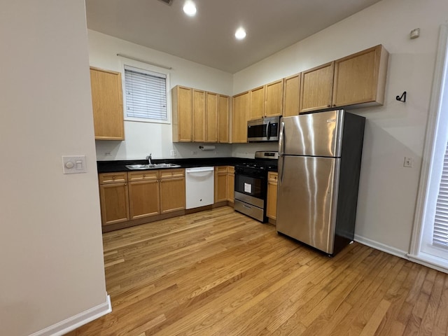 kitchen with appliances with stainless steel finishes, light wood-style flooring, a sink, dark countertops, and baseboards