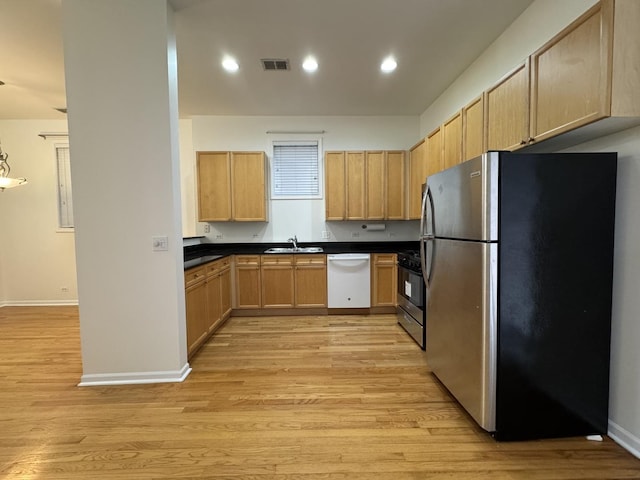 kitchen with stainless steel appliances, a sink, light wood-style floors, light brown cabinetry, and dark countertops