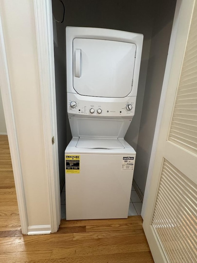 clothes washing area featuring estacked washer and dryer, light wood-style floors, and baseboards