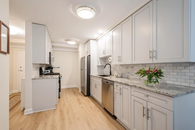 kitchen featuring stainless steel appliances, a sink, decorative backsplash, light wood-style flooring, and baseboards