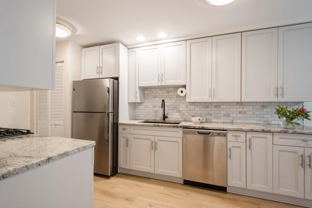 kitchen with appliances with stainless steel finishes, a sink, backsplash, light wood-style floors, and light stone counters