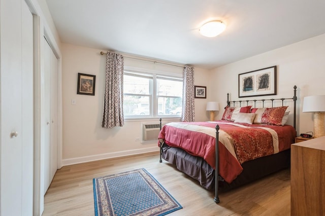 bedroom with light wood-type flooring, a wall unit AC, baseboards, and a closet