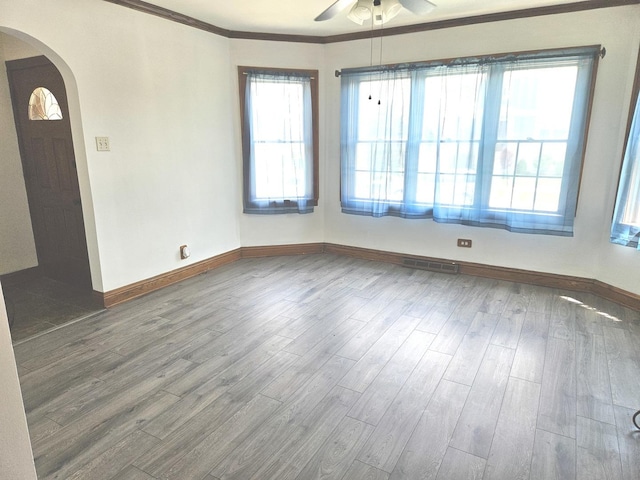 spare room with arched walkways, ceiling fan, wood finished floors, baseboards, and ornamental molding