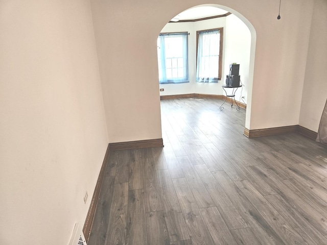 empty room featuring arched walkways, wood finished floors, and baseboards