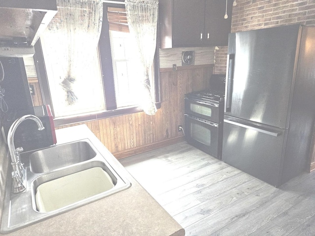 kitchen with freestanding refrigerator, double oven range, a sink, healthy amount of natural light, and wood walls