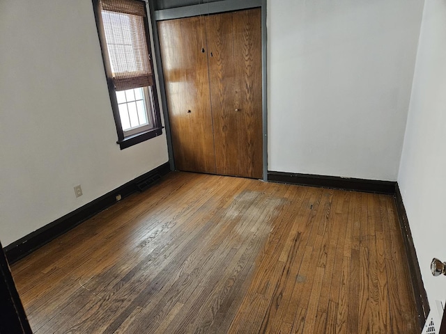 unfurnished bedroom with hardwood / wood-style floors, a closet, and baseboards