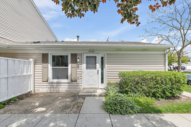 doorway to property featuring fence and a shingled roof