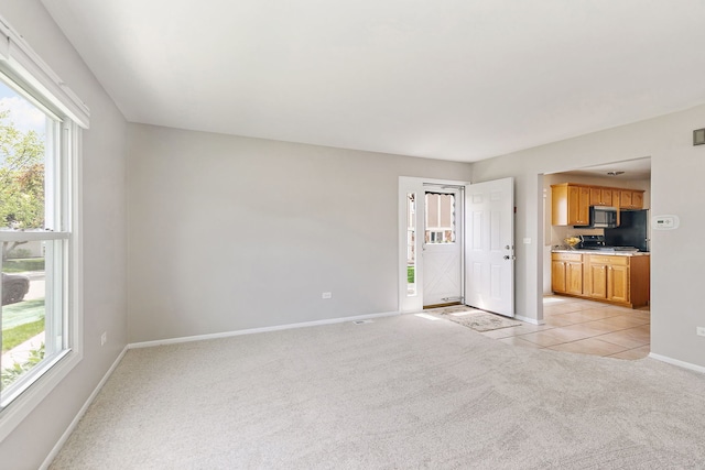 unfurnished living room with light carpet, baseboards, healthy amount of natural light, and light tile patterned floors