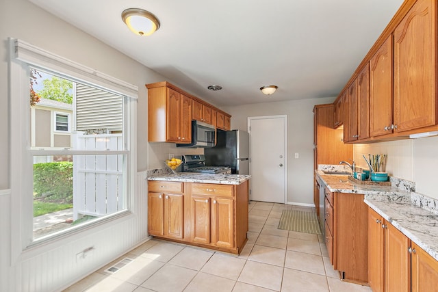 kitchen featuring stainless steel appliances, a sink, light tile patterned flooring, light stone countertops, and brown cabinets