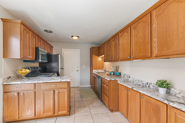 kitchen with appliances with stainless steel finishes, a sink, light tile patterned floors, and light stone counters