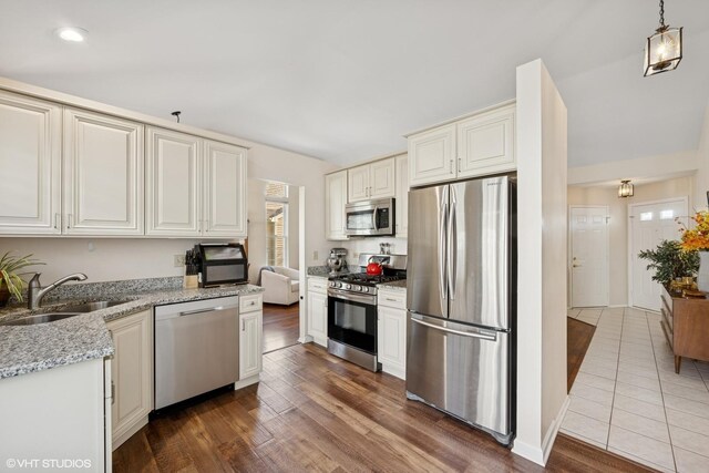 kitchen featuring stainless steel appliances, a sink, light stone countertops, dark wood finished floors, and hanging light fixtures