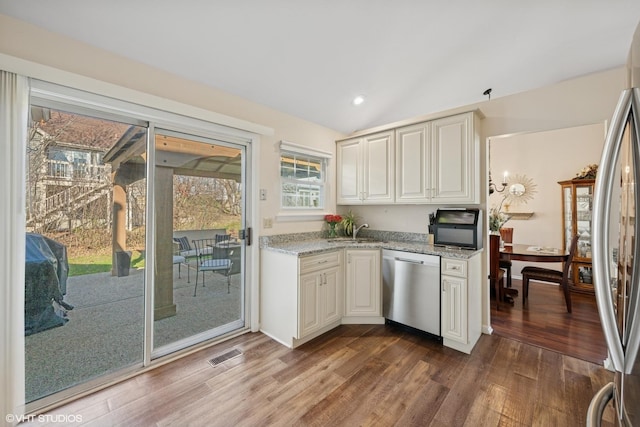 kitchen featuring stainless steel appliances, dark wood finished floors, a sink, lofted ceiling, and light stone counters