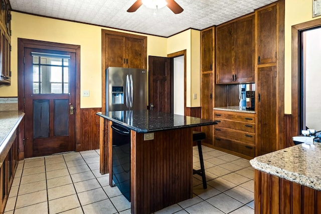 546 Elmwood Ct, El Paso, IL 61738 - kitchen with stainless steel fridge with ice dispenser, wainscoting, light tile patterned floors, ceiling fan, and a kitchen bar