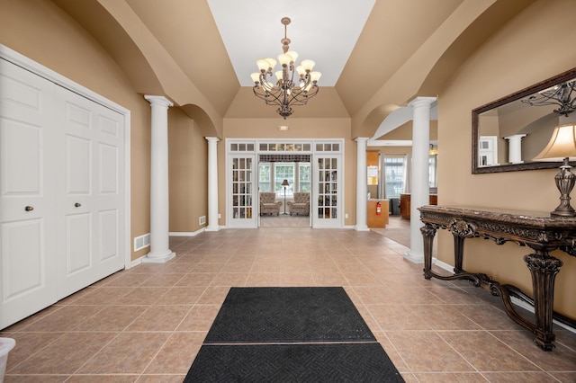 tiled entrance foyer featuring decorative columns, a chandelier, vaulted ceiling, and baseboards
