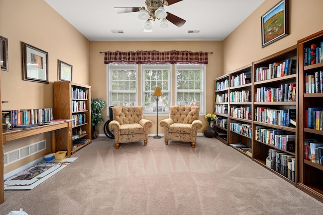 sitting room featuring carpet flooring, ceiling fan, and wall of books