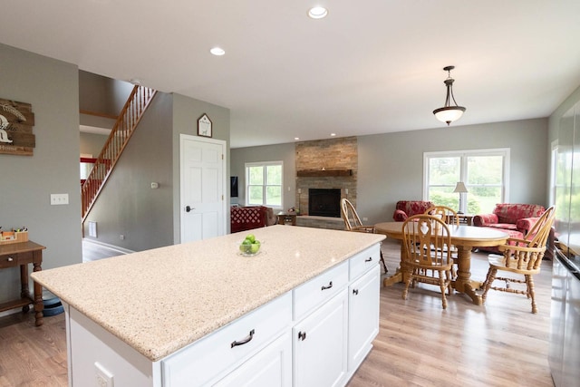 14445 W Walden Ln, Wadsworth, IL 60083 - kitchen featuring a kitchen island, a fireplace, light wood-type flooring, white cabinets, and light stone countertops
