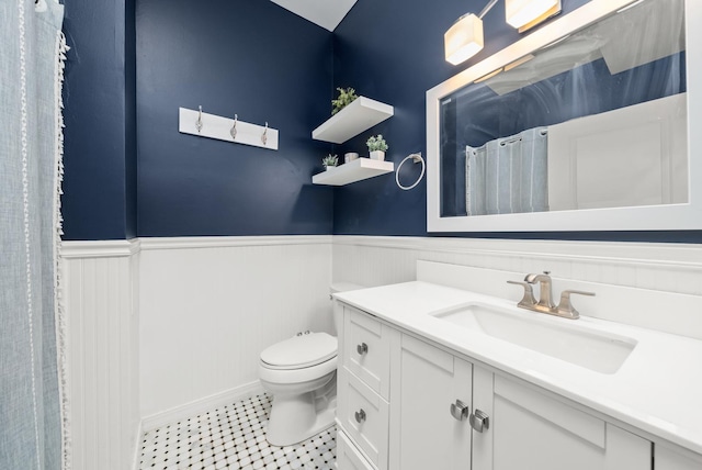 bathroom with a wainscoted wall, toilet, vanity, and tile patterned flooring