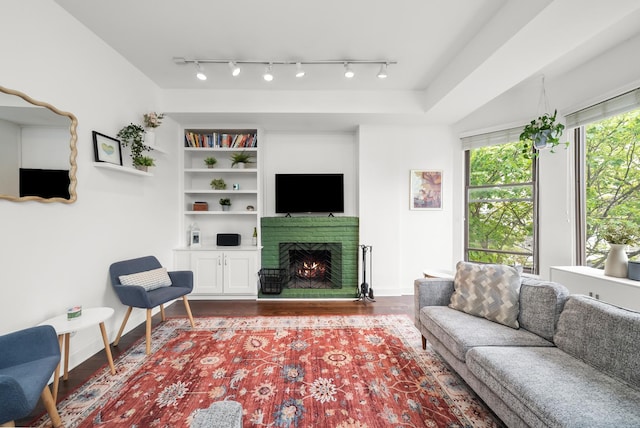 living room with dark wood-style flooring, a brick fireplace, baseboards, and built in shelves