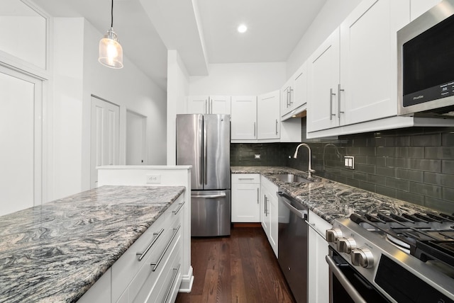 kitchen with appliances with stainless steel finishes, a sink, stone countertops, dark wood-style flooring, and decorative backsplash